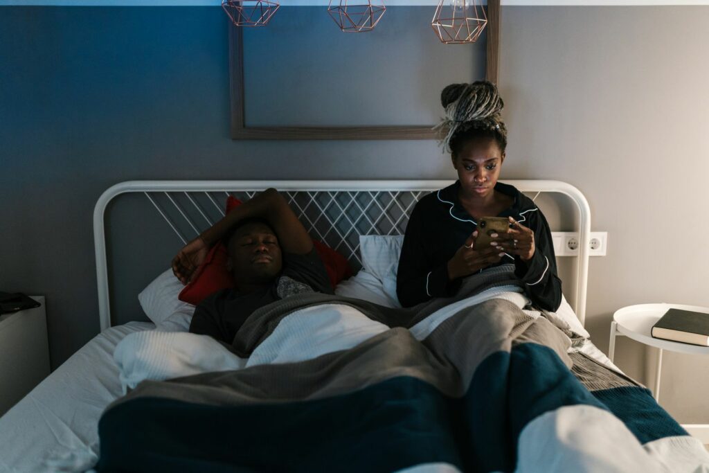 A woman pressing phone on bed beside his sleeping husband